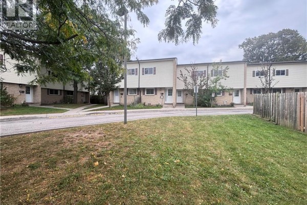 Side view of a townhouse complex showing multiple units with grass and pavement in the foreground. - 211 Veronica Drive Unit# B24, Kitchener