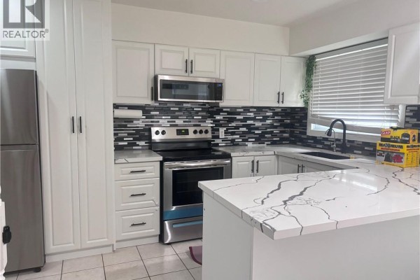 Modern white kitchen with stainless steel appliances, black and white mosaic tile backsplash, and a large island. - 211 Veronica Drive Unit# B24, Kitchener