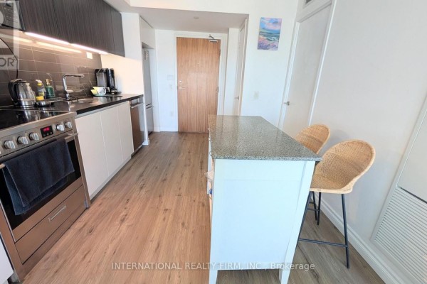 A living area with a grey sectional sofa, a wooden coffee table, and a kitchen in the background. - 2110 - 85 Queens Wharf Road, Toronto