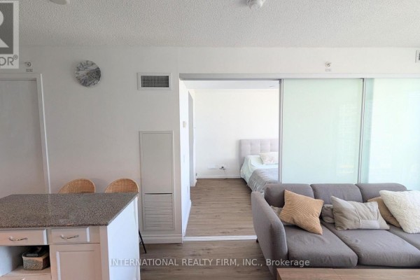 A living room with a grey sectional sofa, a coffee table, and a large window with city views. - 2110 - 85 Queens Wharf Road, Toronto
