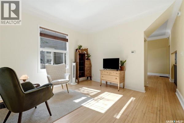 Living room with light wood floors, cream walls, a television, and vintage furniture. - 2112 Wallace Street, Regina