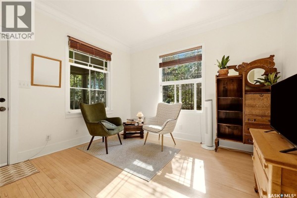 Living room with two chairs, a small table, a vintage dresser, and two windows. - 2112 Wallace Street, Regina