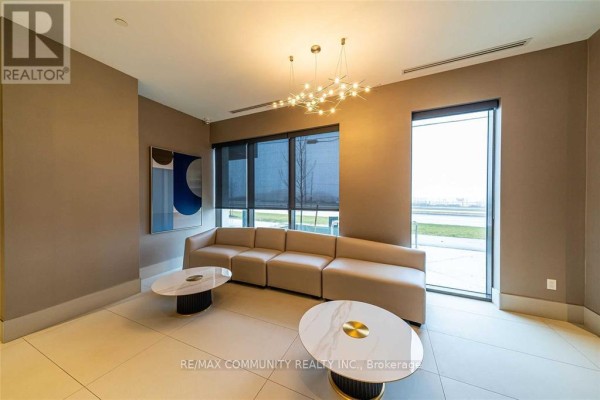 Building lounge area with a curved beige sofa, two marble coffee tables, and large windows. - 2114 - 2550 Simcoe Street N, Oshawa