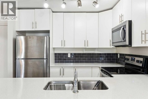 Kitchen sink area with a stainless steel double basin sink, chrome faucet, and white quartz countertops. - 2115, 181 Skyview Ranch Manor Ne, Calgary