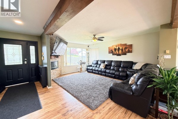 Living room with black leather sectional, grey rug, stone fireplace, and wood floors. - 2116 Northland Rd, Port Mcneill