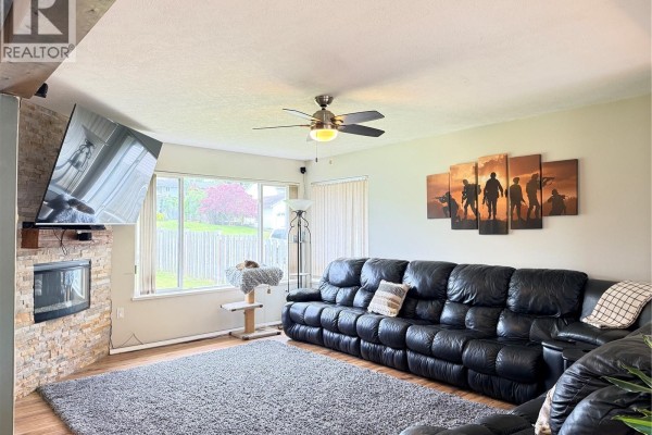 Living room fireplace with stone surround, black leather sectional, and large window. - 2116 Northland Rd, Port Mcneill