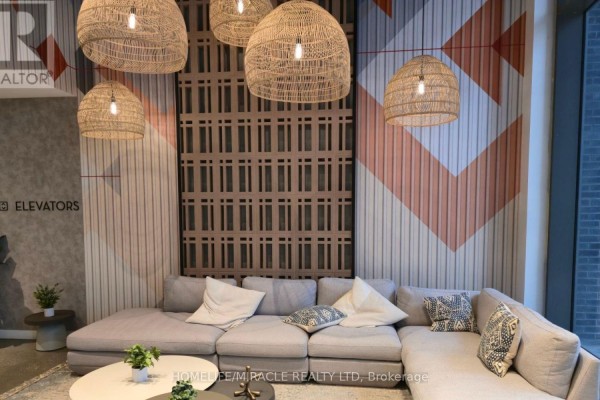 A cozy seating area with a sectional sofa, woven pendant lights, and decorative wall art. - 2118 - 10 Abeja Street, Vaughan