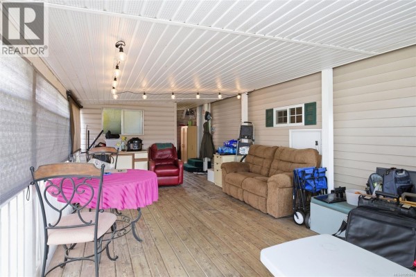 Covered wooden deck with furniture including a round table with chairs and a sofa. - 2118 Buttle Lake Way, Nanaimo