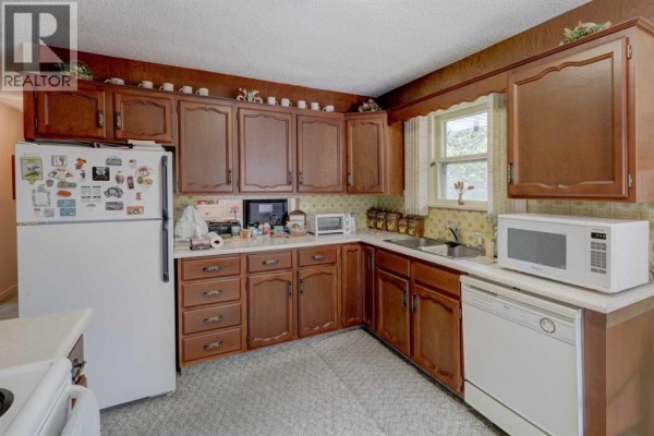 Kitchen with dark wood cabinets, white refrigerator, dishwasher, and a patterned backsplash. - 2119 Halifax Crescent Nw, Calgary