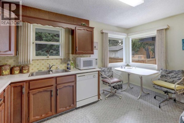 Kitchen area with a sink, dishwasher, microwave, and a small table with chairs. - 2119 Halifax Crescent Nw, Calgary
