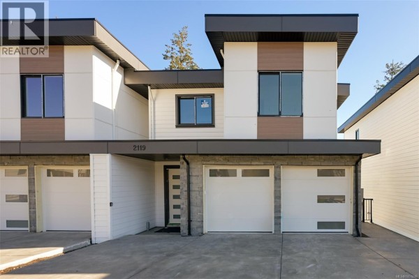 Front exterior of a modern duplex with white siding, grey stone accents, and two garages. - 2119 Kingbird Dr, Langford