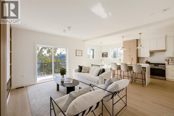 Open concept living and kitchen area with light wood floors, white cabinets, and island seating. - 2119 Kingbird Dr, Langford