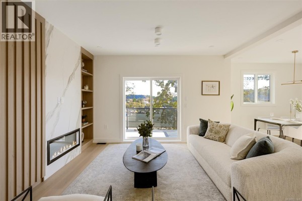 Living room with a gas fireplace, built-in shelves, beige sofa, and large sliding glass door. - 2119 Kingbird Dr, Langford