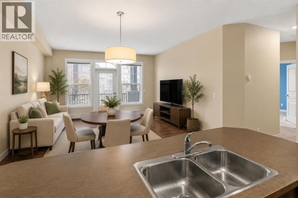 Kitchen with dark wood cabinets, black appliances, a double sink, and a hallway visible. - 212, 10 Panatella Road Nw, Calgary