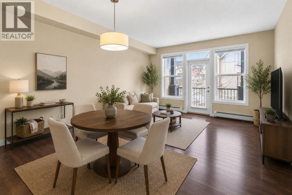 View from the kitchen island showing a sink, with living area and balcony visible through glass doors. - 212, 10 Panatella Road Nw, Calgary