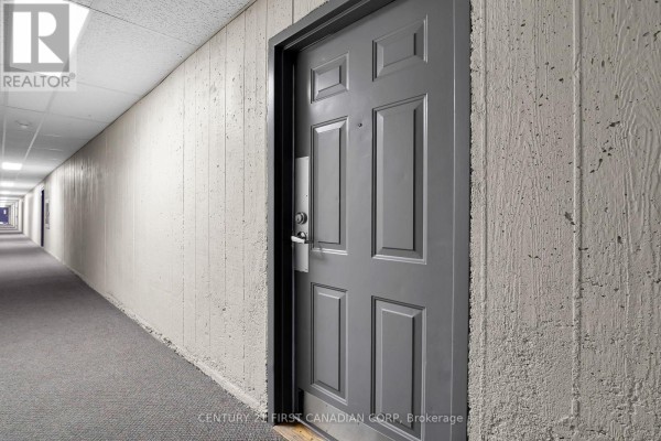 Exterior view of a beige apartment building with a parking lot. - 212 - 1447 Huron Street, London East