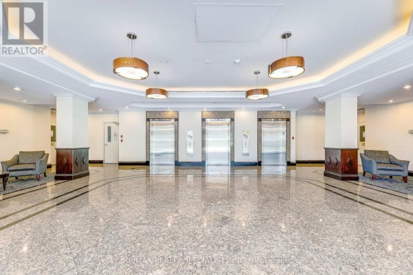 Modern building lobby with polished grey marble floors, three elevators, and two plush armchairs. - 212 - 2155 Burnhamthorpe Road W, Mississauga