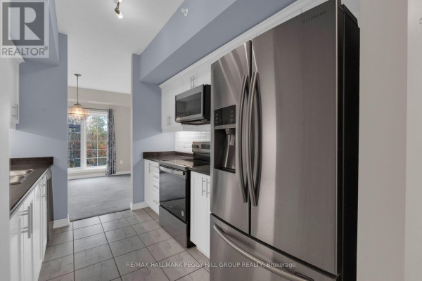 Kitchen with stainless steel refrigerator, white cabinets, and dark countertops. - 212 - 5 Greenwich Street, Barrie