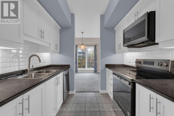 Galley kitchen with white cabinets, stainless steel appliances, and view into dining area. - 212 - 5 Greenwich Street, Barrie