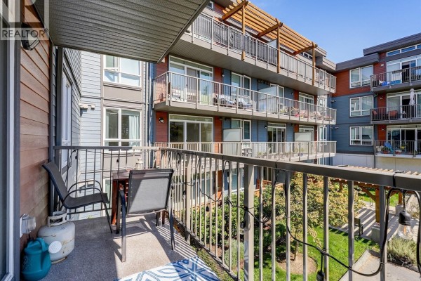 Apartment balcony with two chairs, a table, and a propane tank. - 212 110 Presley Pl, View Royal