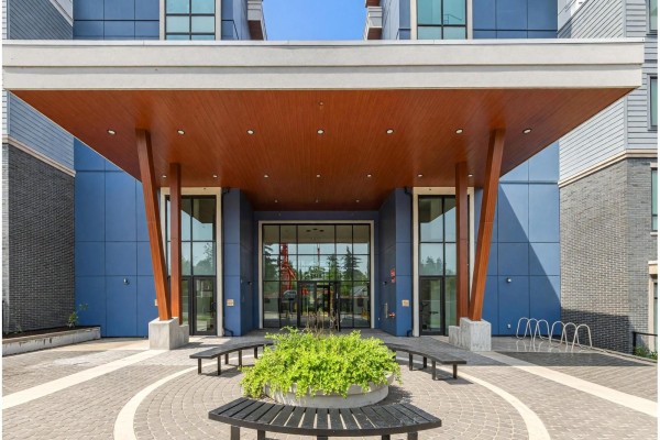 Close-up of the modern building entrance with a wood-paneled ceiling and glass panels. - 212 6220 Gooseberry Drive, Surrey