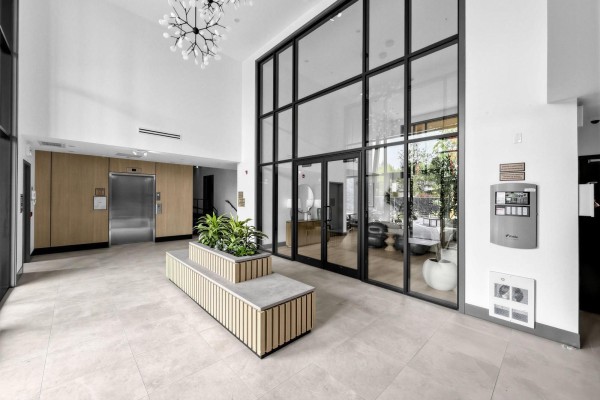 Apartment building lobby with polished floors, elevator, and large glass windows. - 212 6220 Gooseberry Drive, Surrey