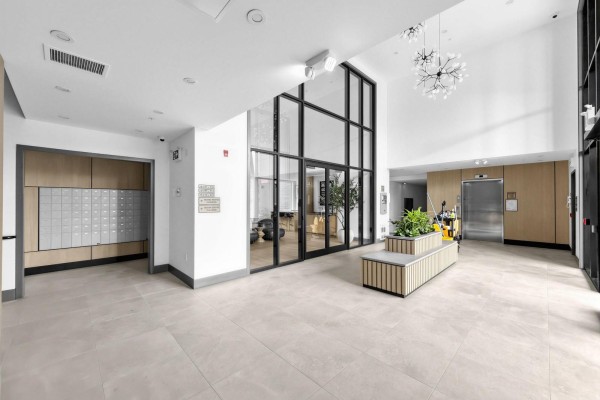 Spacious apartment building lobby with mailboxes, seating, elevator, and large glass walls. - 212 6220 Gooseberry Drive, Surrey