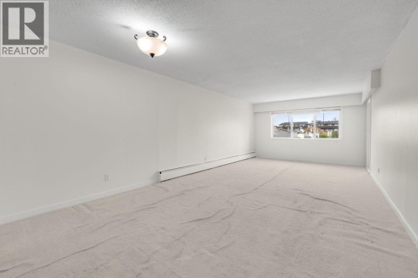 Living room with beige carpet, white walls, and a large window with a view. - 212 6420 Buswell Street, Richmond