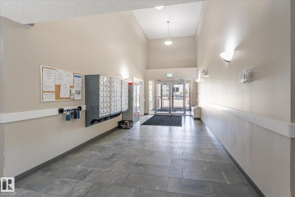 Apartment building lobby with gray tile floors, mailboxes, and bulletin boards. - #212 6925 199 St Nw, Edmonton