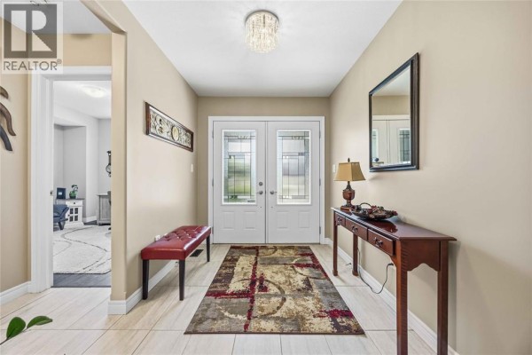 Interior foyer with cream-colored walls, beige tiled floor, double glass doors, and a red bench. - 212 Basquiat Crescent, Sarnia