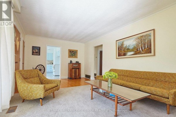 Living room with a yellow sofa, armchair, coffee table, and wood radio cabinet. - 212 Hallett Avenue, Whitby