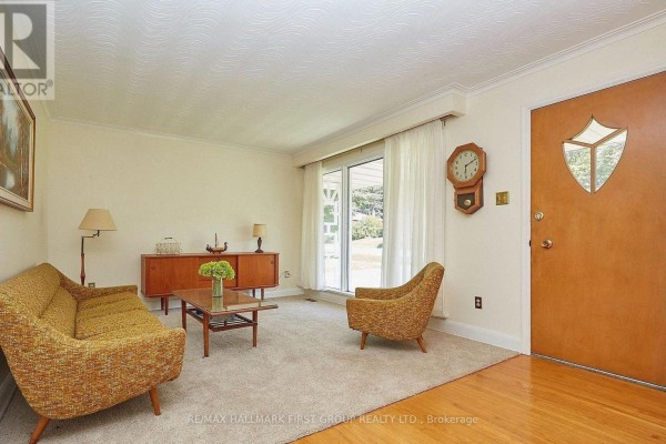 Living room showing the sofa, armchair, coffee table, and wooden door. - 212 Hallett Avenue, Whitby