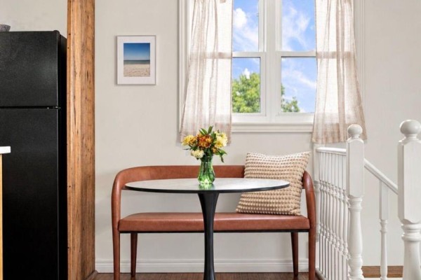 Interior view of a small dining nook with a brown curved bench, round table, and white window curtains. - 212 Old Milford Road, Prince Edward County