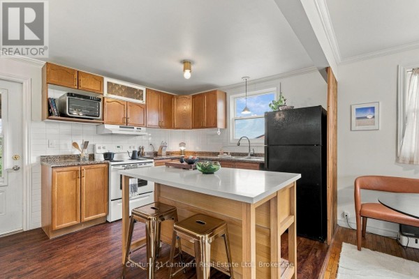 Kitchen with light wood cabinets, white quartz island with two stools, and dark wood floors. - 212 Old Milford Road, Prince Edward County