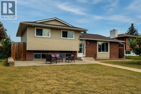 Side view of a split-level house with brick and vinyl siding, a paved walkway and lawn. - 212 Pinetree Place Ne, Calgary