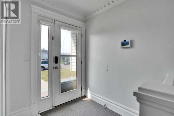 Interior view of a beige entryway with a double glass door and gray carpet. - 212 Pinetree Place Ne, Calgary