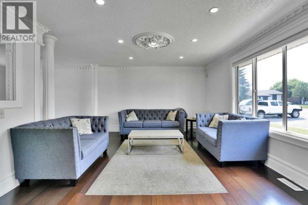 Living room with three blue tufted sofas, a light wood coffee table, and dark hardwood floors. - 212 Pinetree Place Ne, Calgary