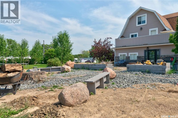 Backyard view showing a gravel area with large boulders, a concrete bench, and unfinished landscaping. - 212 Prospect Street, Belle Plaine