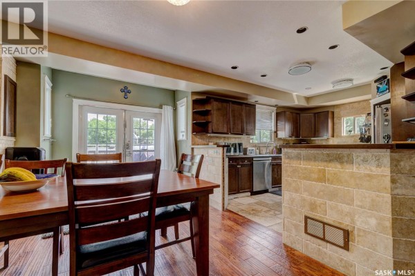 Dining area with a wooden table and chairs, adjacent to a kitchen with dark wood cabinets and stainless steel appliances. - 212 Prospect Street, Belle Plaine