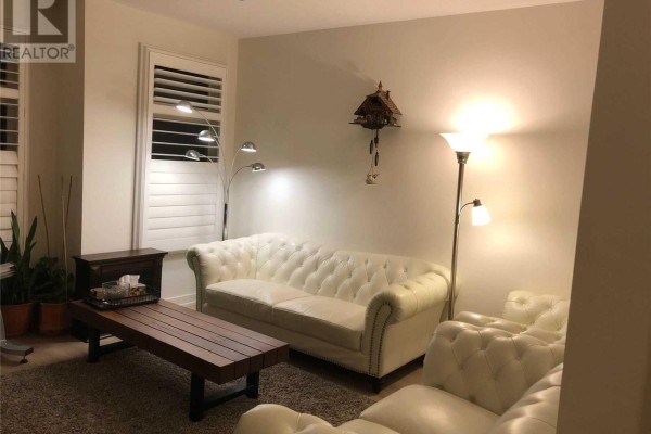 Living room with two white tufted sofas, a dark wood coffee table, and white plantation shutters on the windows. - 212 Squire Crescent, Oakville