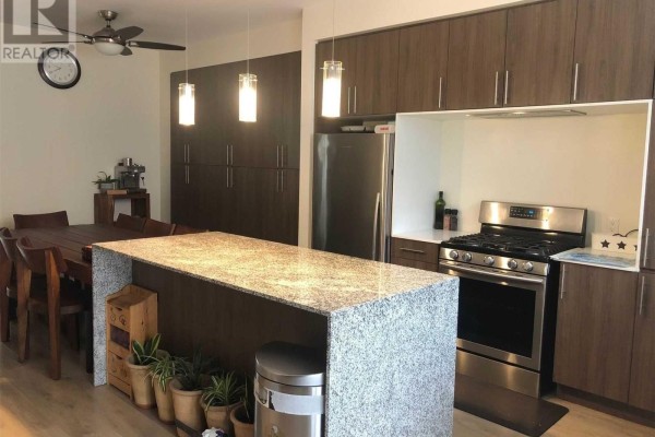 Kitchen and dining area featuring a granite-topped island, dark wood cabinetry, stainless steel appliances, and a wooden dining set. - 212 Squire Crescent, Oakville