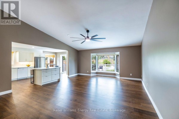 Living area with hardwood floors, vaulted ceiling, bay window, and view of the kitchen. - 212 Wilmot Trail, Clarington