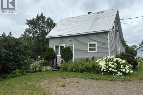 Grey house with a metal roof and landscaping featuring white hydrangeas. Cloudy sky. - 2123 Sainte-louise, Sainte Louise