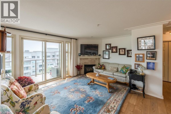 Living room with fireplace, sofa, coffee table, and large blue rug. - 2125 Atkinson Street Unit# 901, Penticton