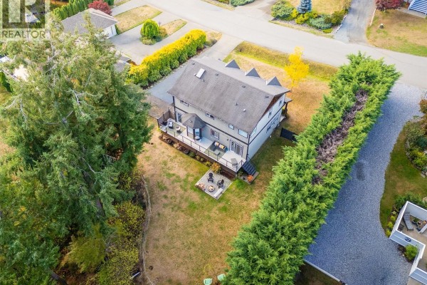 Aerial view of the back of the house showing a deck, backyard, and surrounding trees. - 2125 Wildflower Rd, Shawnigan Lake
