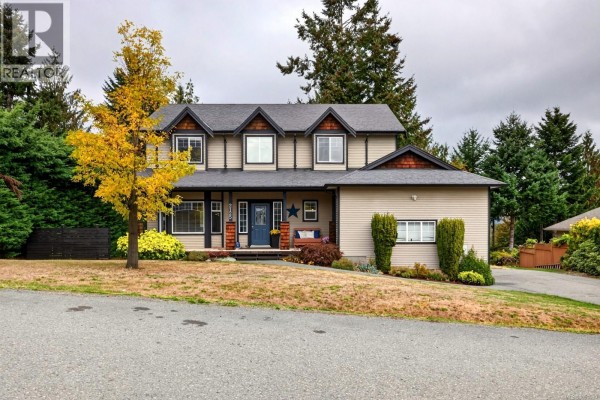 Front exterior of the beige house with a covered porch and landscaping. - 2125 Wildflower Rd, Shawnigan Lake