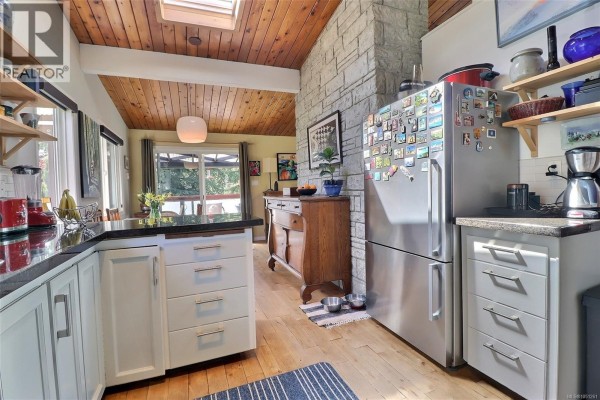 View of a spacious kitchen with stainless steel refrigerator, wooden ceiling, stone accent wall, and granite countertops. - 2128 Calais Rd, Duncan