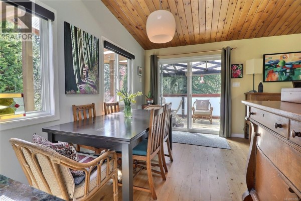 A dining area with a dark wood table, chairs, and sliding glass doors leading to an outdoor patio. - 2128 Calais Rd, Duncan
