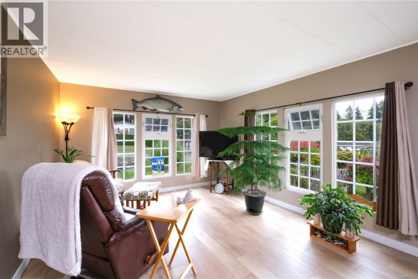Living room with tan walls, large windows, a brown recliner, plants, and a fish mounted on the wall. - 2129 Rama Rd, Campbell River