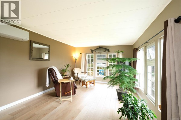 Living room with tan walls, a recliner, a large plant, and windows offering views of the outdoors. - 2129 Rama Rd, Campbell River